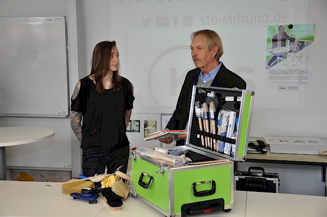 Regina Geist nimmt ihren neuen Werkzeugkoffer von Uwe Koos (Sto-Stiftung) in Empfang